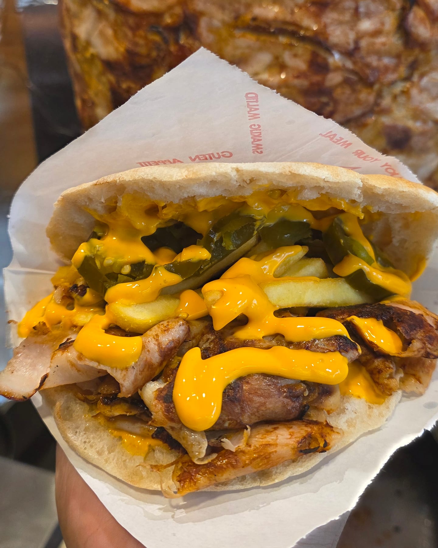 Chilli-Cheese Döner im Fladenbrot, in der Hand vor dem Hähnchenspieß