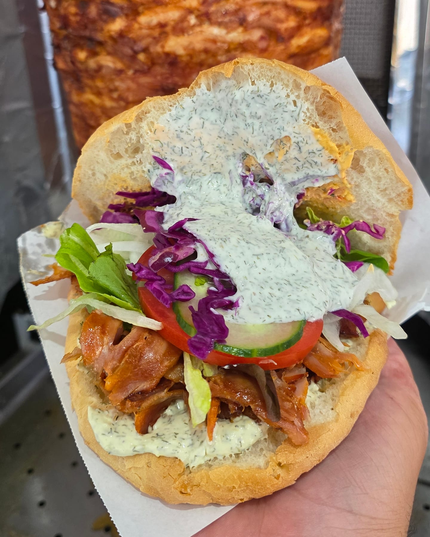 Döner mit Rotkraut, Salat, Gurke und Kräutersoße, dahinter der Spieß