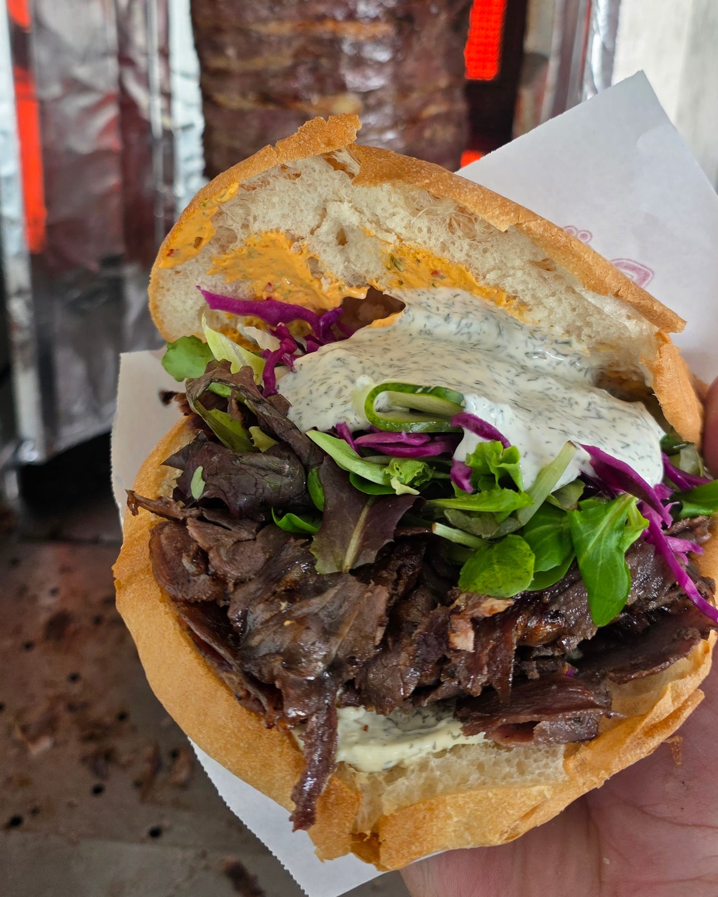 Döner mit Steakfleisch, Salat und Kräutersoße vor dem glühenden Grill